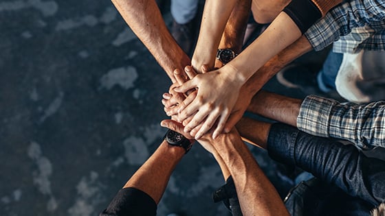 All hands in. The FundApps team works together to help solve issues in your compliance process. Hands stacked upon one another, showing teamwork.