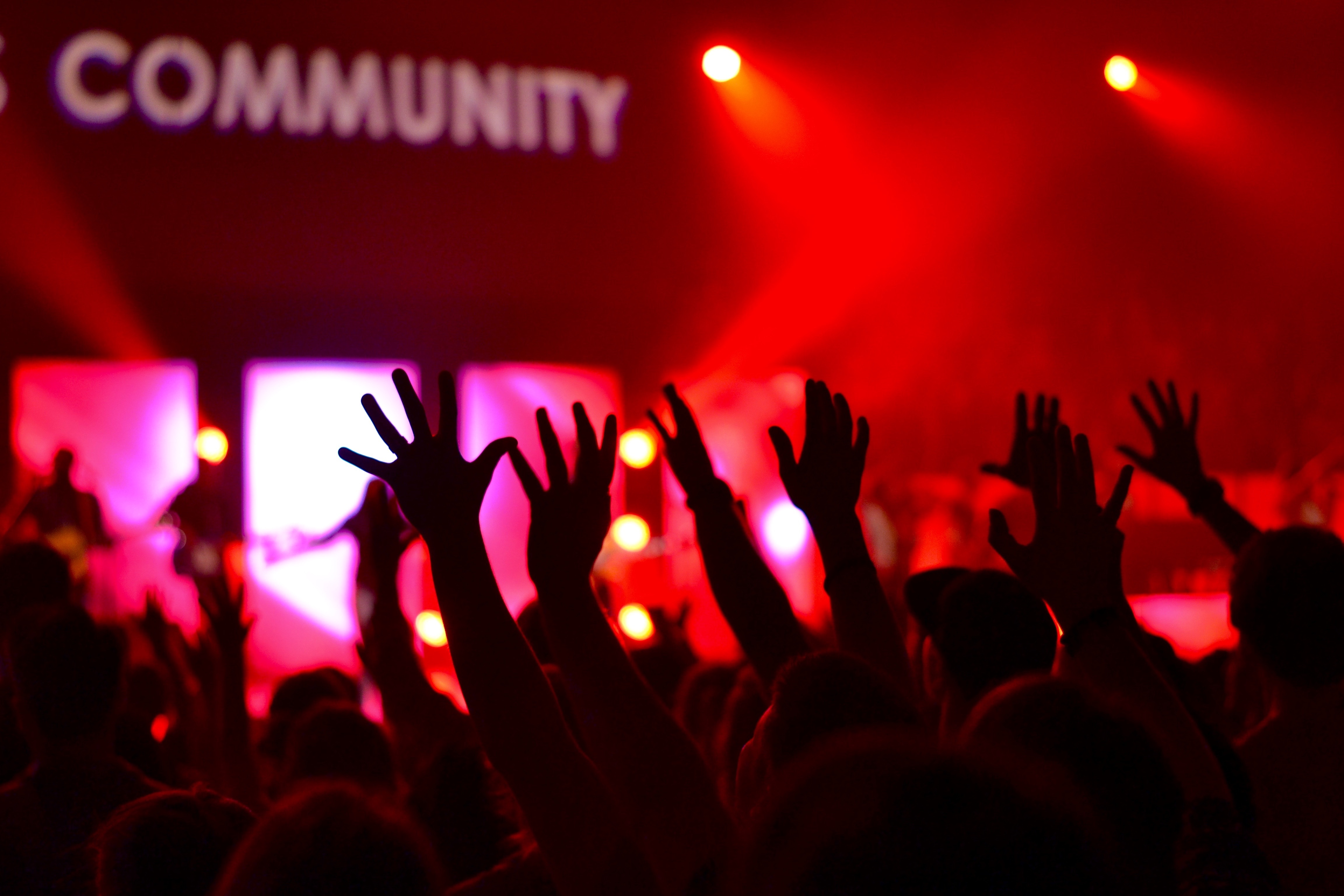 An image of hands in the air during concert with red stage lighting and 'community' written on the stage. Rave about the power of FundApps community. 