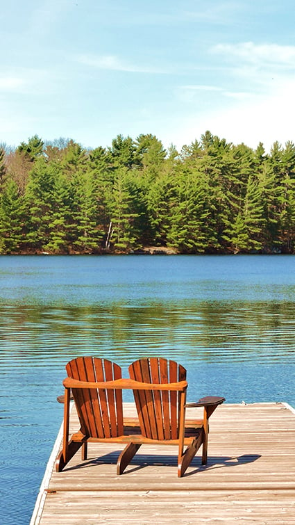 Two lounge chairs facing a lake and trees. 