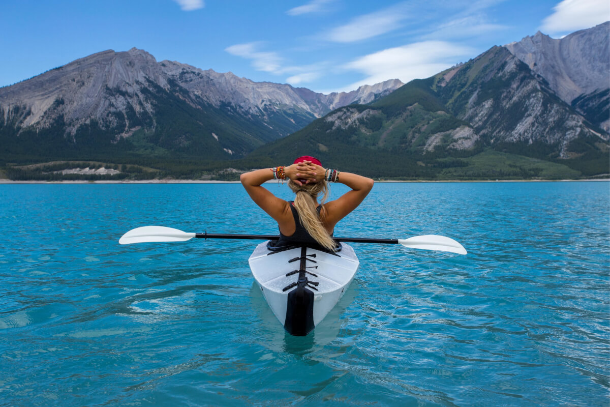 Woman on a rowboat relaxing, staring at mountains. Sit back and unwind, as at FundApps we have got you covered when responding to regulatory change.