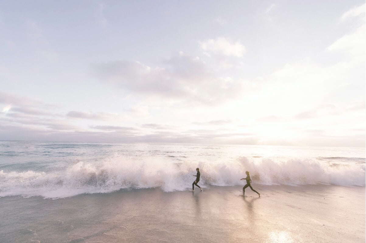 Just like surfers, FundApps ride the wave amongst any firms, large or small.  Two surfers walking the beach as a wave comes in. 